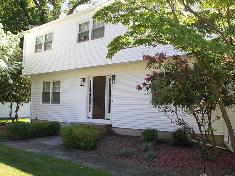 A white house featuring large vinyl windows with newly installed vinyl siding, showcasing a modern and energy-efficient exterior