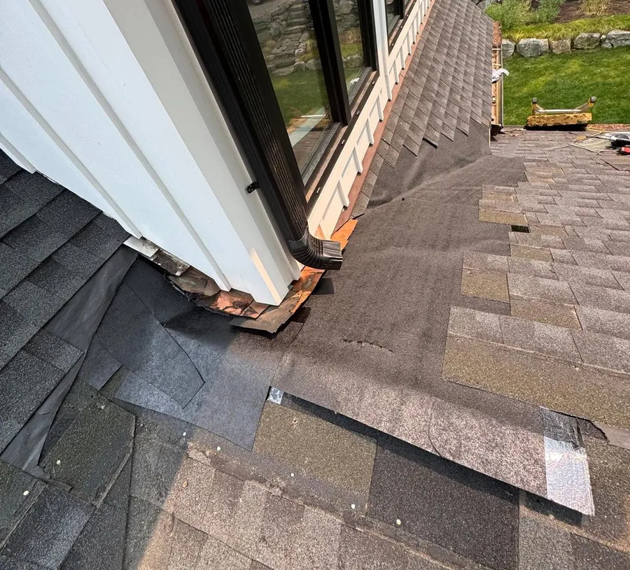 Roof repair in progress showing exposed underlayment, removed shingles, and roof-to-wall flashing areas